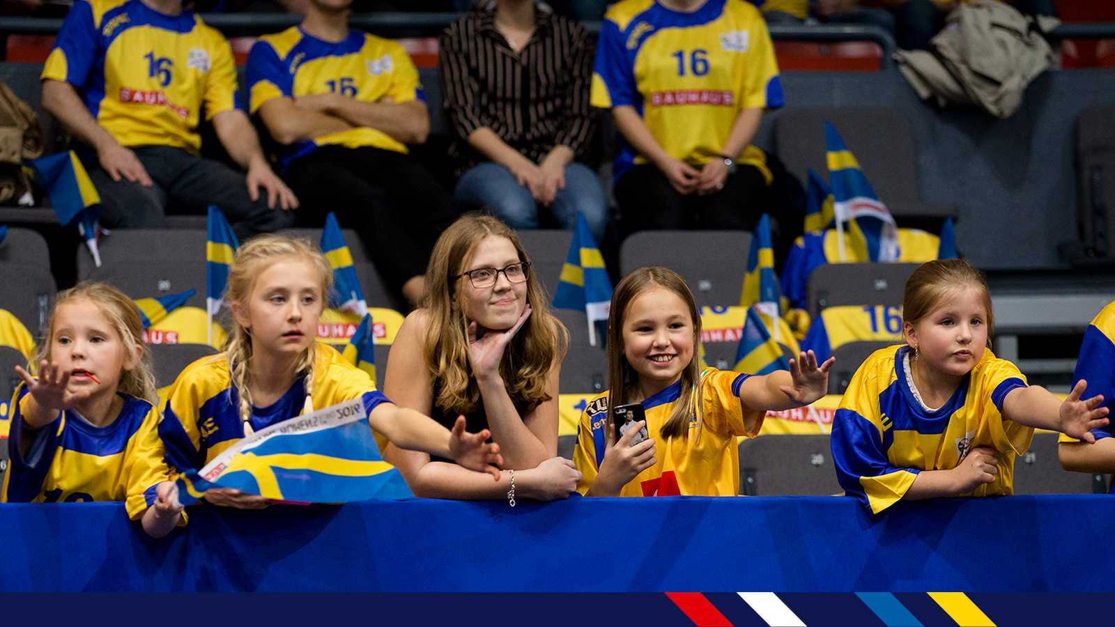 unga tjejer med sverigetröjor och en liten sverigeflagga inne i en arena