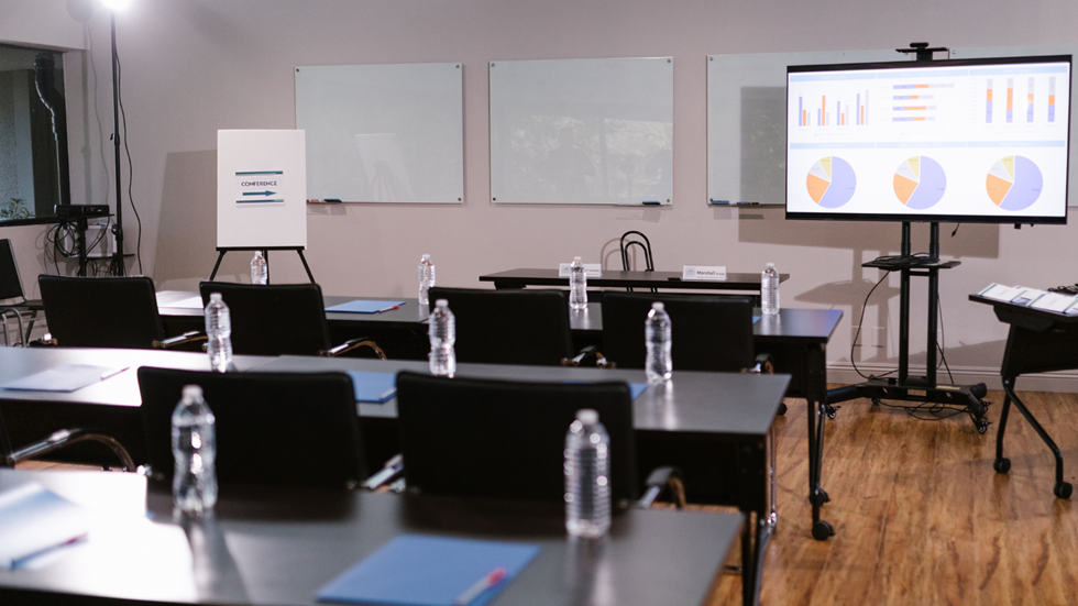 Ett tomt konferensrum med en vattenflaska vid varje plats och en stor skärm med en presentation på längst fram